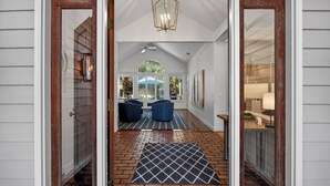 Un hall d’entrée spacieux avec un sol en briques, un tapis à motifs et un coin salon avec des chaises bleues.