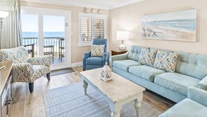 Un salon avec vue sur l’océan, un fauteuil bleu, un canapé bleu clair et une table basse en bois.