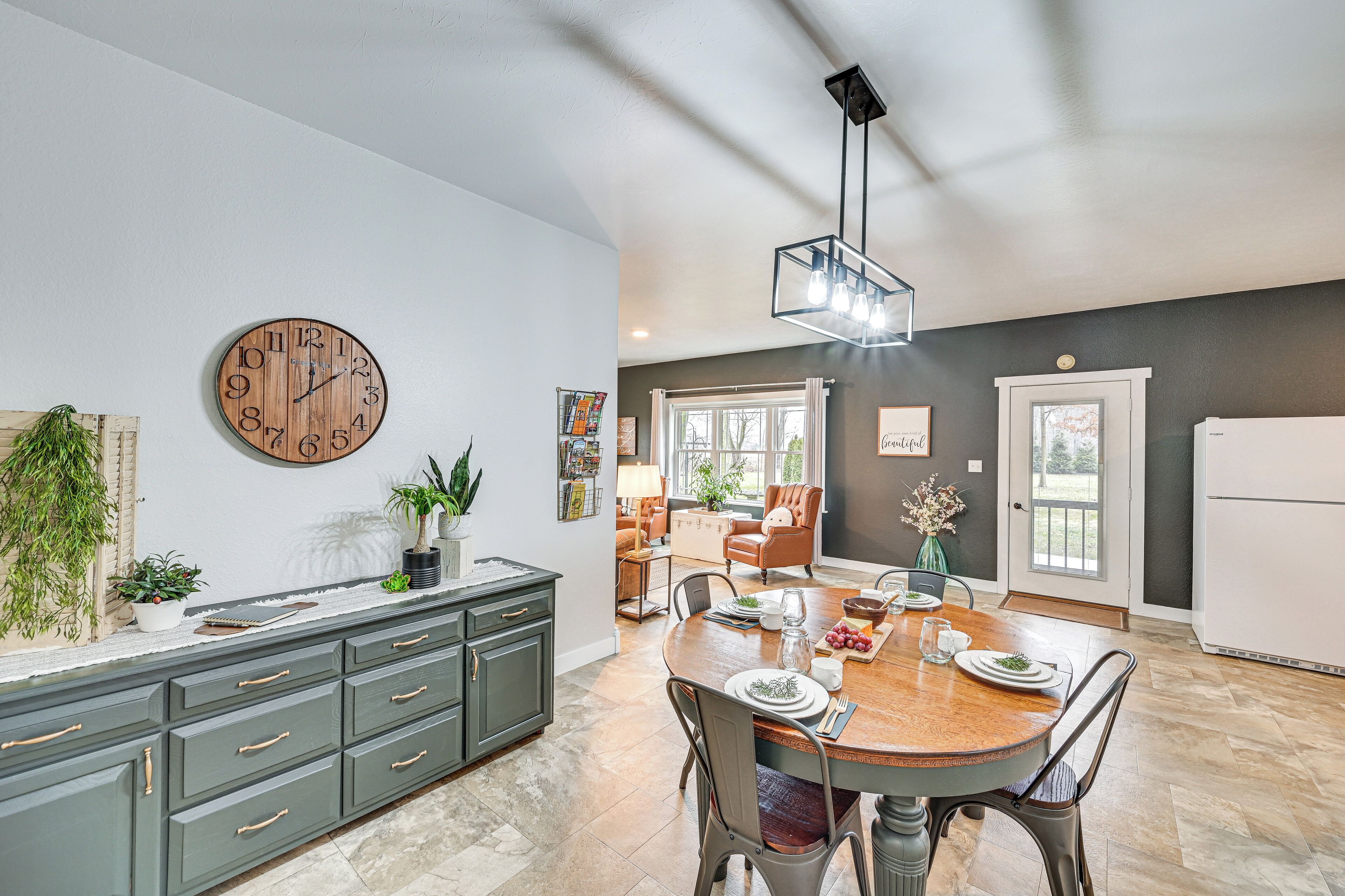 A modern kitchen with a wooden clock, grey cabinetry, and a dining area with a wooden table and chairs.