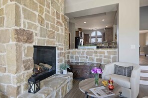 A stone fireplace, a sofa, a coffee table, and a kitchen in the background. - Lazy Getaway on The Cove | Concierge Services (Kingsland)