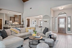 A spacious living room with a sectional sofa, a coffee table with decorative items, and a view into the kitchen area. - Lazy Getaway on The Cove | Concierge Services (Kingsland)