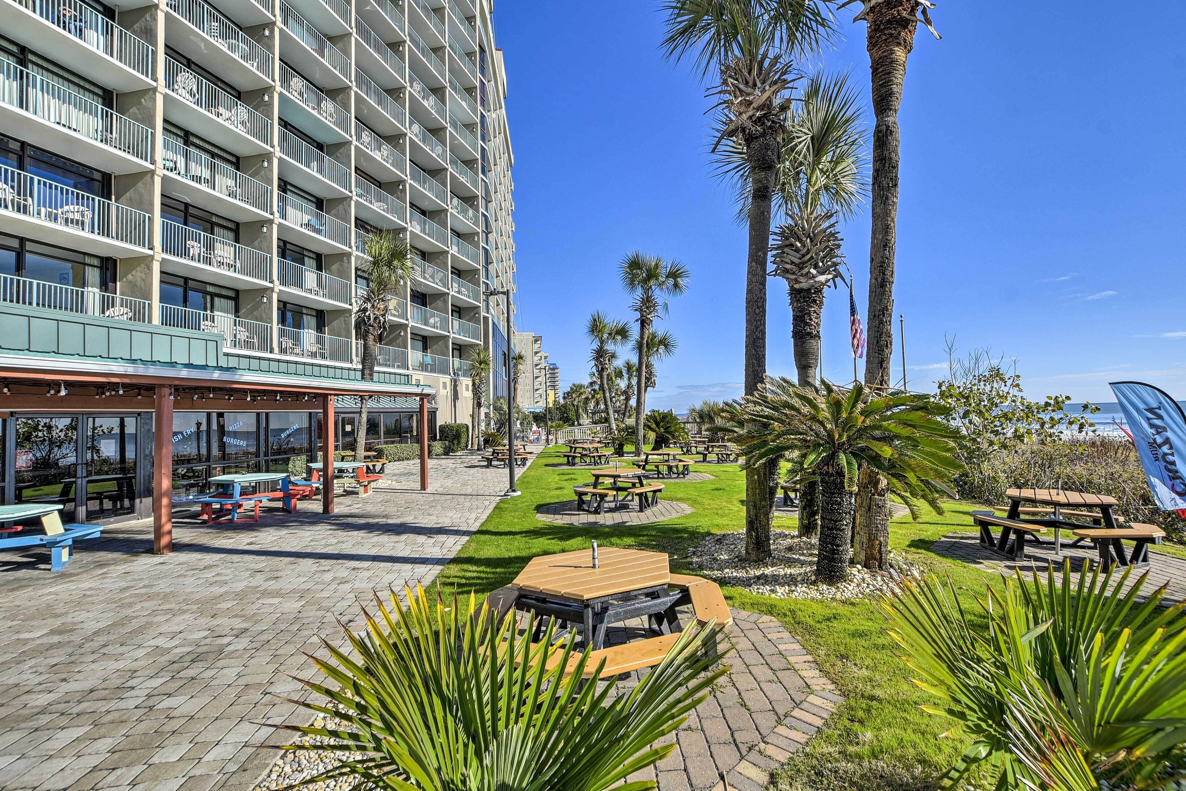 A hotel courtyard with outdoor seating, palm trees, and a building with balconies.