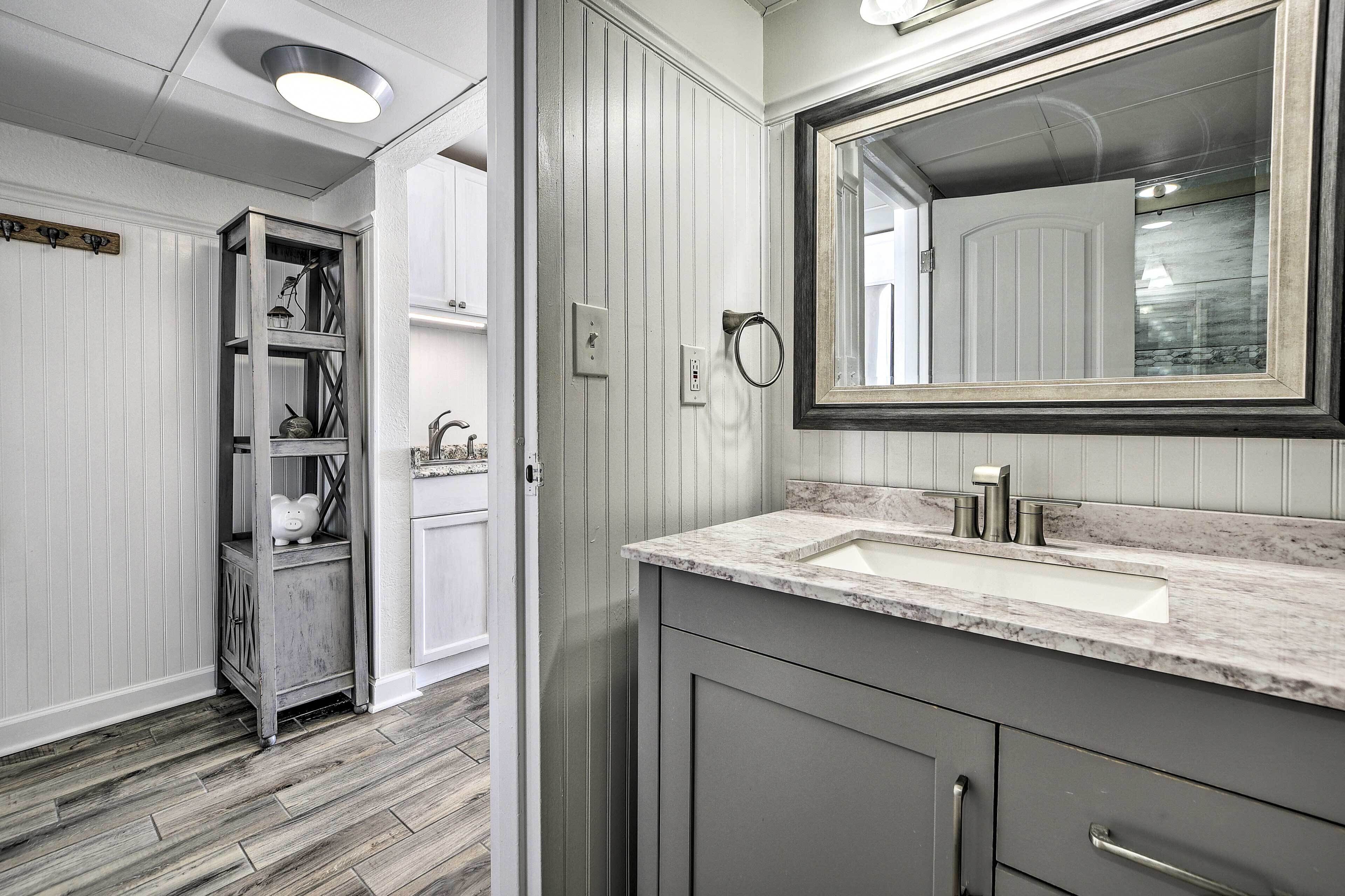 A bathroom with a white vanity, a large mirror, and a wooden shelf unit.