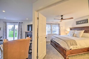 A bedroom with a bed, a ceiling fan, a fireplace, and a view of the outdoors.
