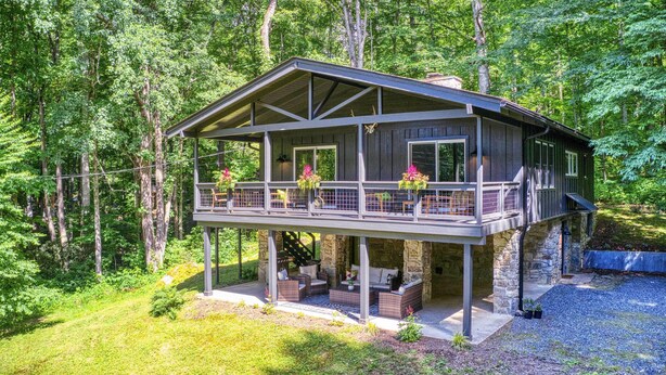 A two-story cabin with a balcony, stone foundation, and outdoor seating area. - Maggie Valley ‘Creekside Chalet’ + Deck: Fish, Ski (Maggie Valley)