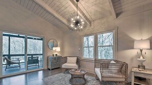 A spacious room with a large sliding glass door leading to a deck, a round wicker coffee table, wicker chairs, a small side table with a lamp, and a ceiling light fixture. - Maggie Valley ‘Creekside Chalet’ + Deck: Fish, Ski (Maggie Valley)
