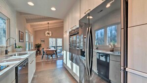 A modern kitchen with stainless steel appliances, a dining area with a wooden table and chairs, and large windows providing natural light. - Maggie Valley ‘Creekside Chalet’ + Deck: Fish, Ski (Maggie Valley)