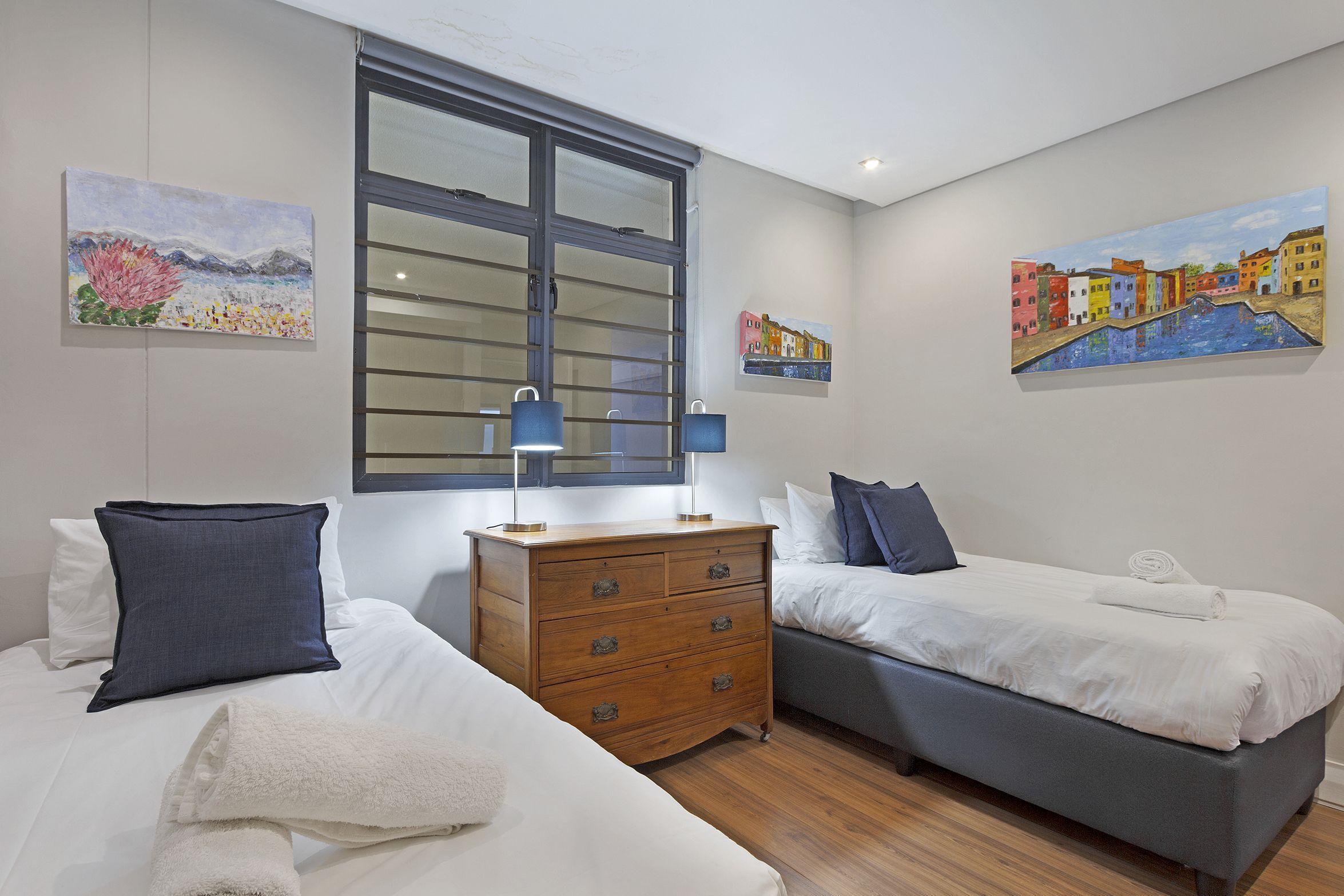 A hotel room with two beds, a dresser, and artwork on the walls.