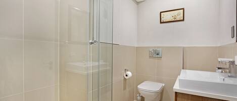 A modern bathroom with a glass shower enclosure, a toilet, and a sink with a wooden cabinet.