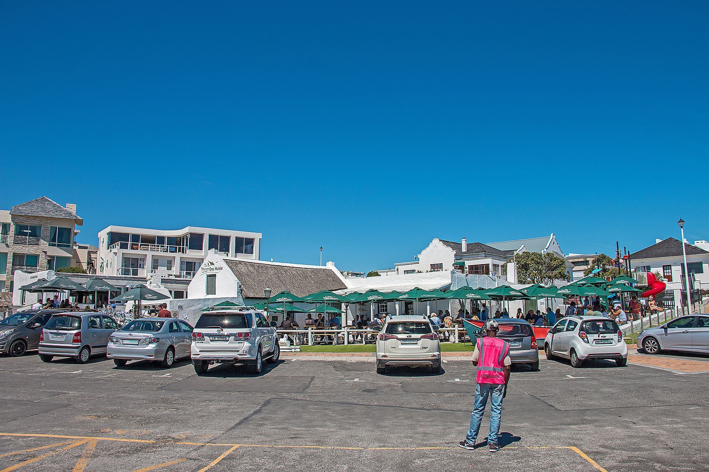 A parking lot with several cars and a person in a pink vest standing.