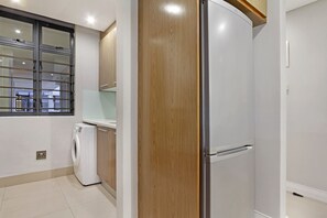 A compact kitchen with a washing machine, a refrigerator, and wooden cabinets. - Eden on the Bay 171 (Cape Town)
