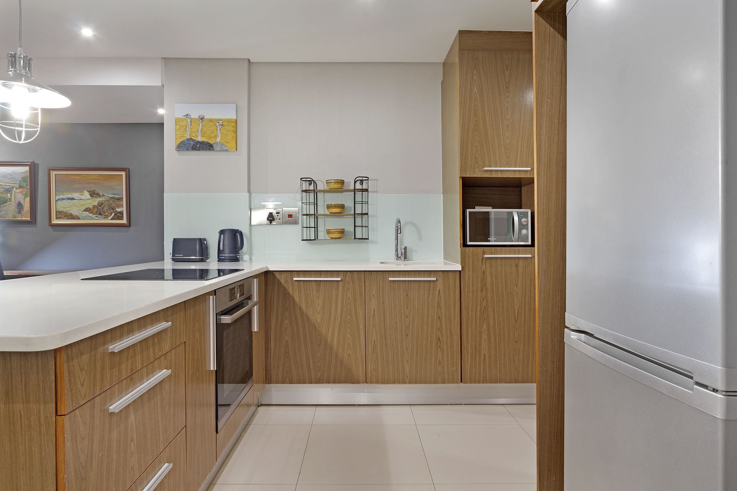 Une cuisine moderne avec des meubles en bois, un plan de travail blanc, un four encastré, un four à micro-ondes et un évier.