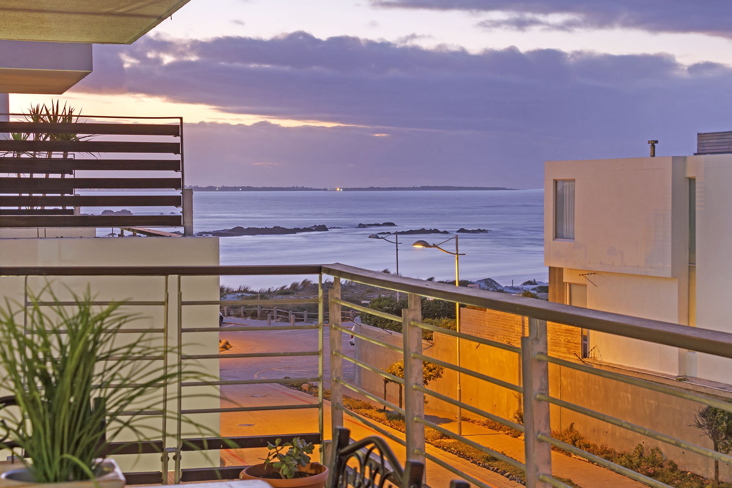 A balcony with a view of the sea, a railing, and a potted plant.