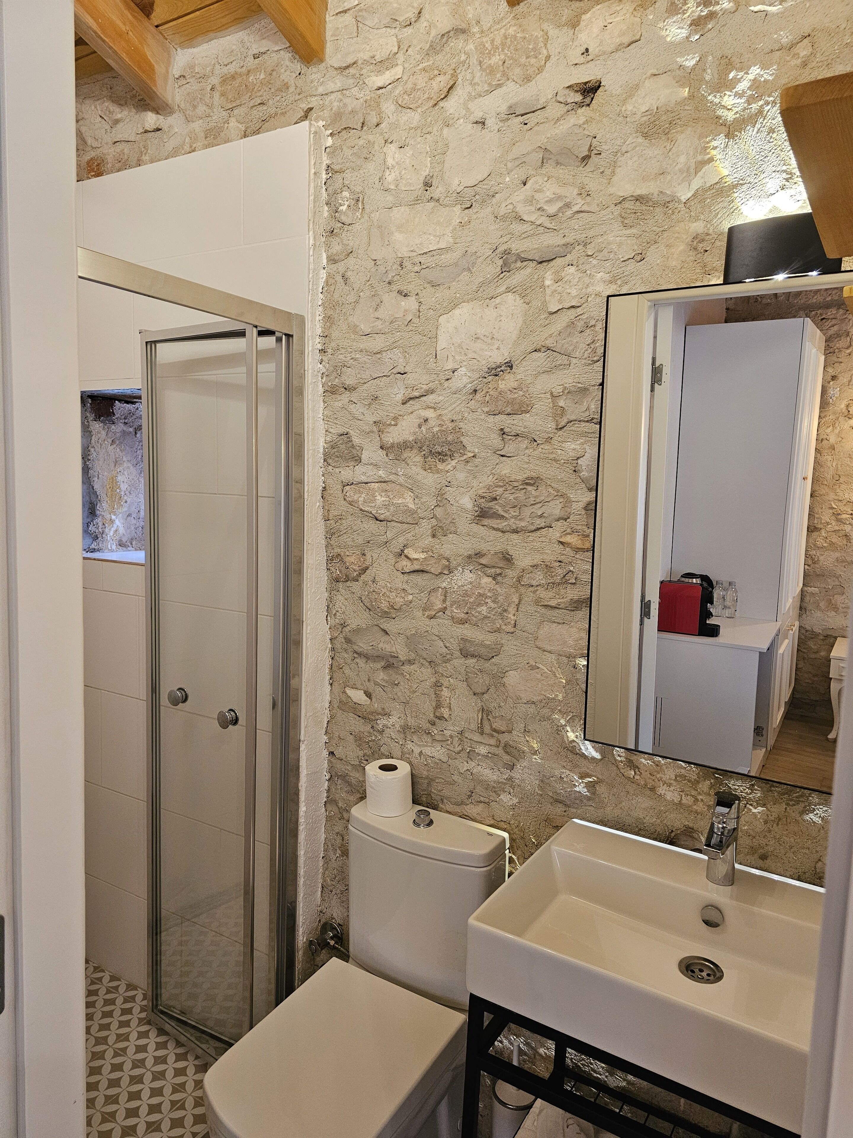 A bathroom with a stone wall, a glass shower enclosure, a toilet, and a sink with a mirror above it.