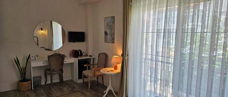 A hotel room with a bed, a desk with a chair, a TV, a lamp, and a large window with curtains.