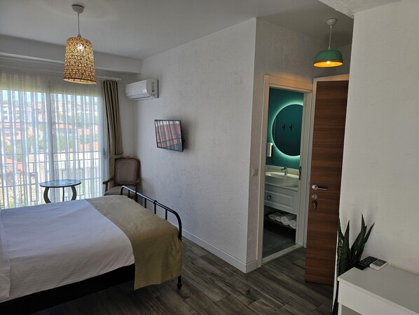 A hotel room with a bed, a chair, a TV, and a bathroom with a mirror and sink.
