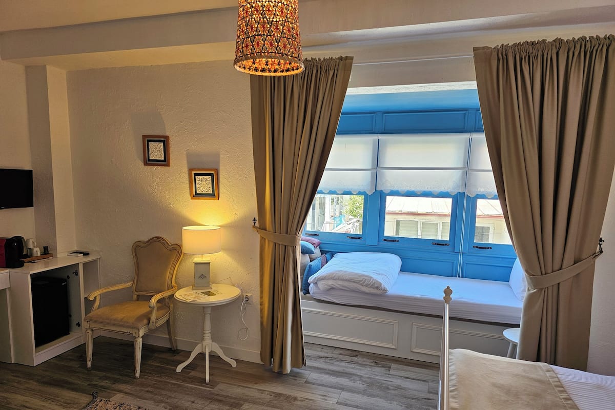 A hotel room with a bed, a desk with a lamp, a chair, and a window with curtains.