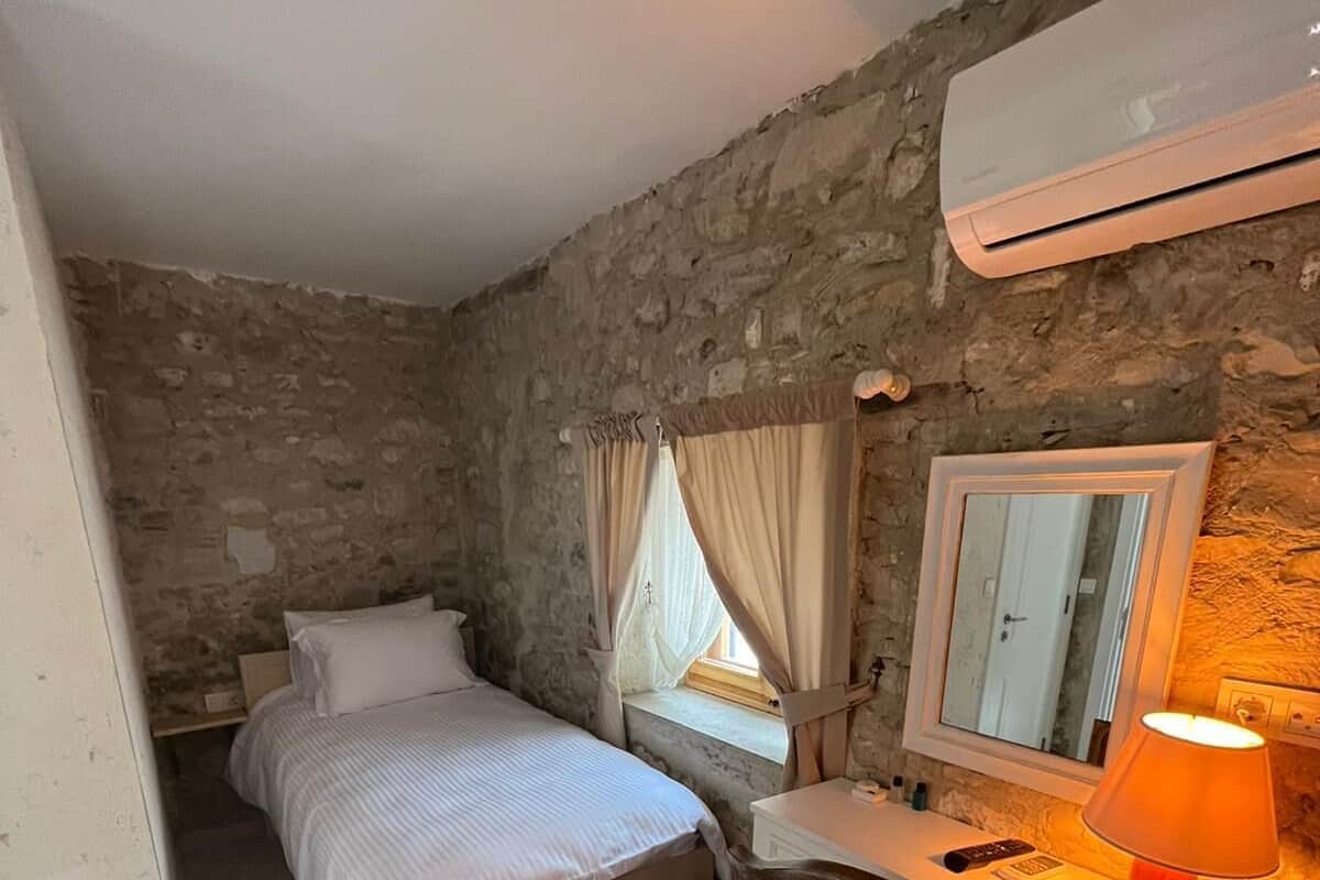 A bedroom with a bed, a desk, a chair, a mirror, and an air conditioning unit.