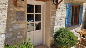 Un edificio de piedra con una puerta blanca, un cartel que indica los tipos de habitación y un banco de madera en el exterior.