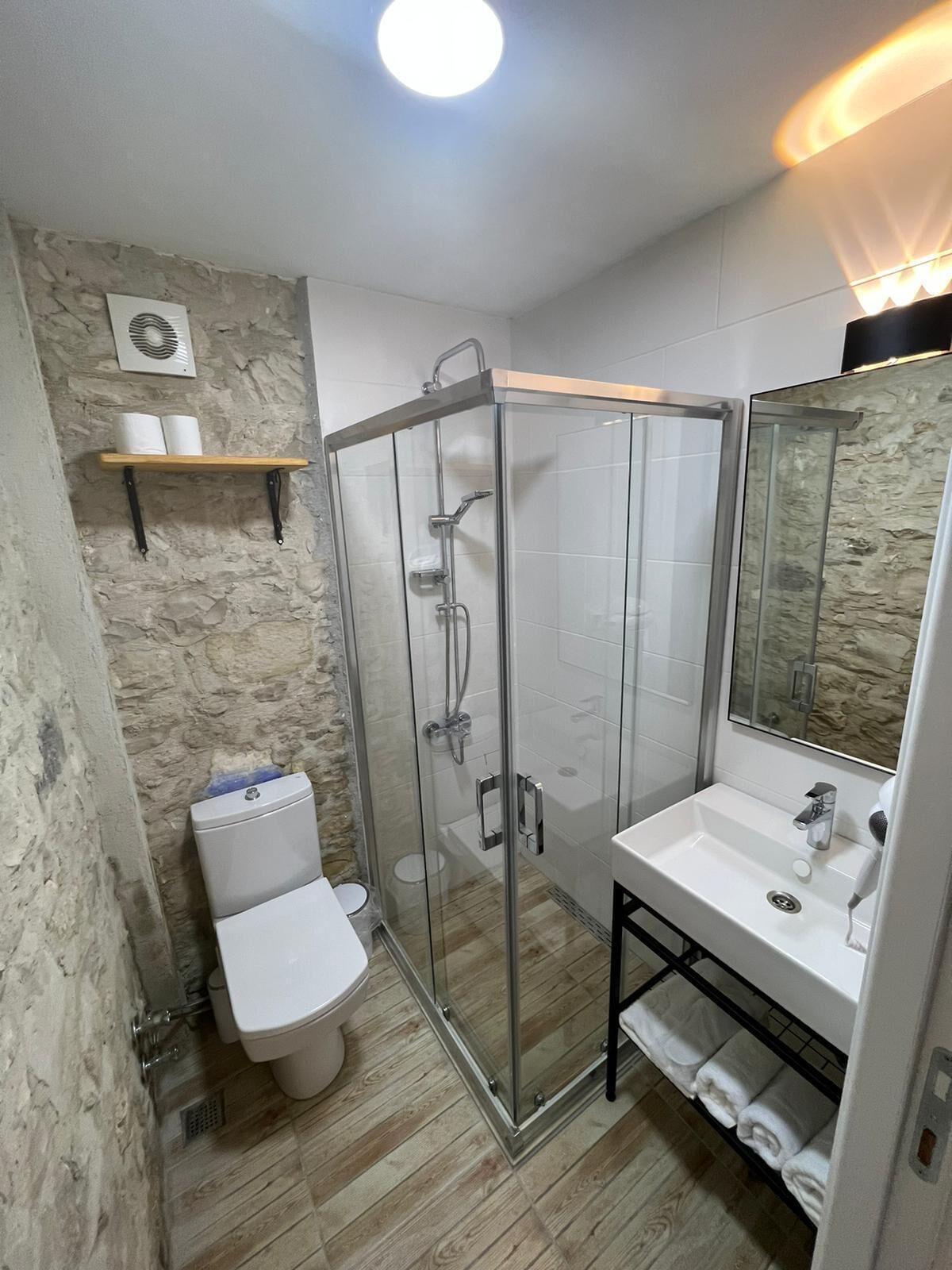 A modern bathroom with a glass-enclosed shower, a white toilet, and a sink with a towel rack.