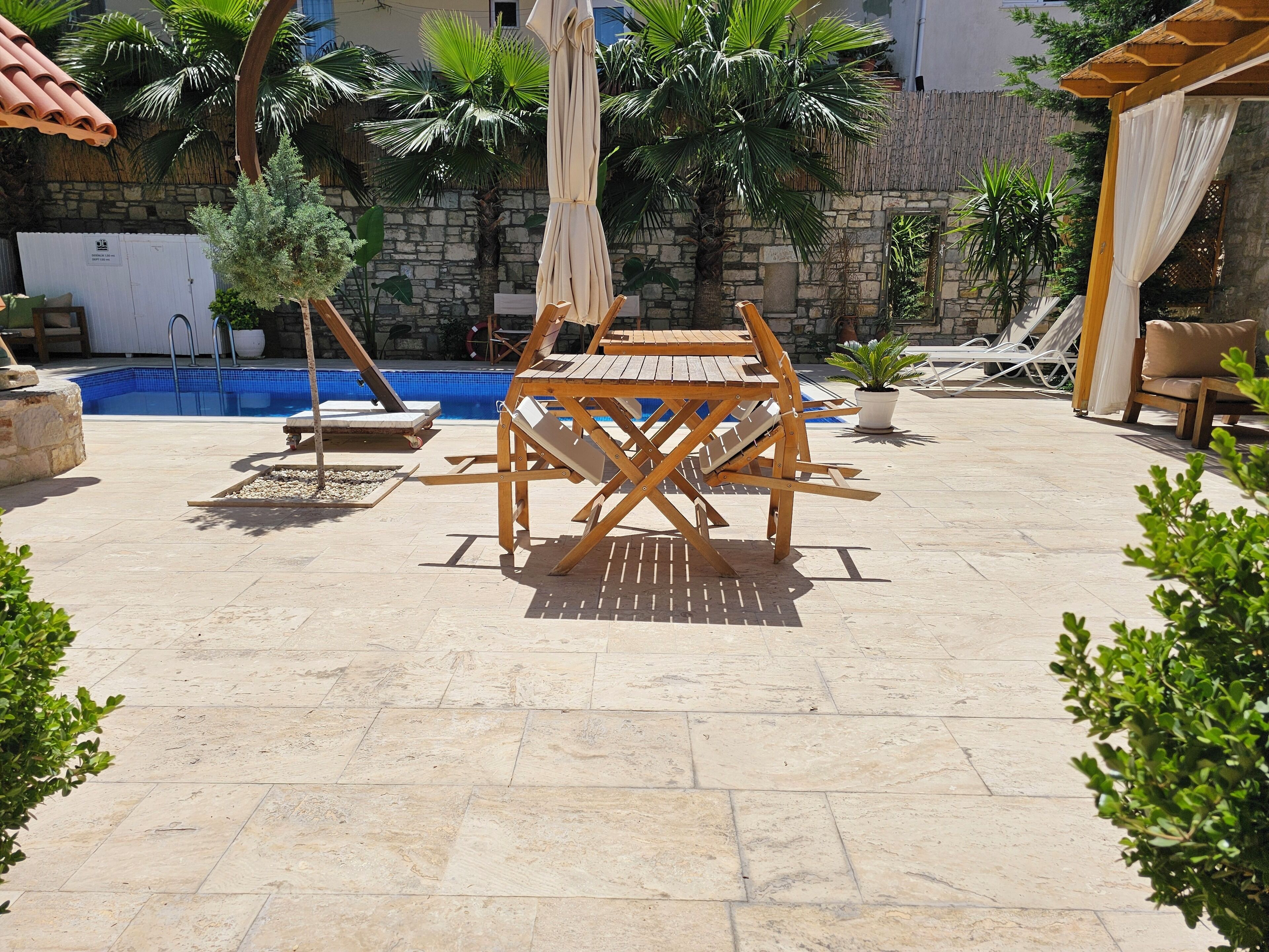 An outdoor patio with a pool, wooden furniture, and potted plants.
