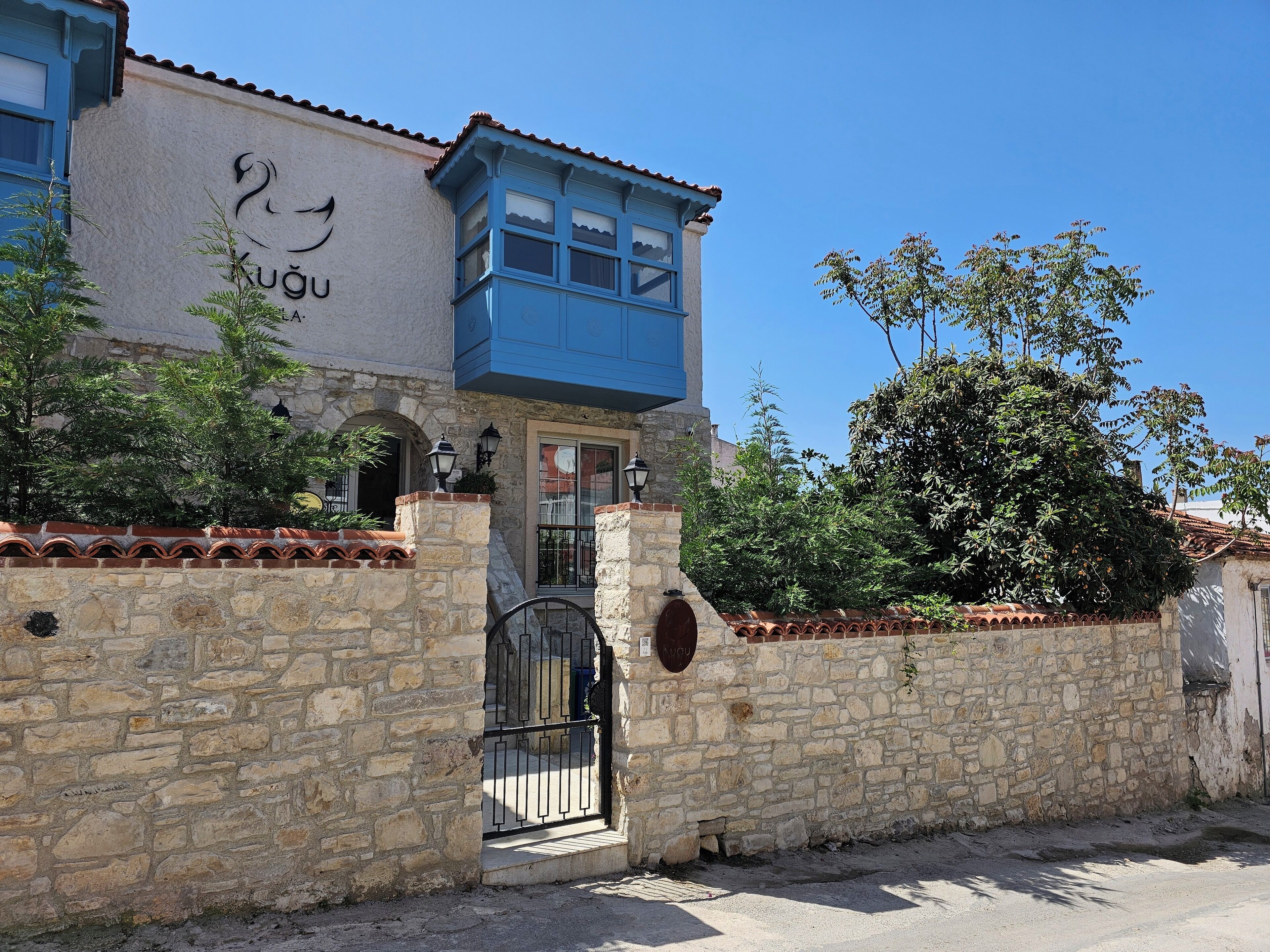 A stone building with a blue upper section, a sign with a bird and text, and a gate.