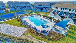 A resort with a large pool, sun loungers, and a tennis court.