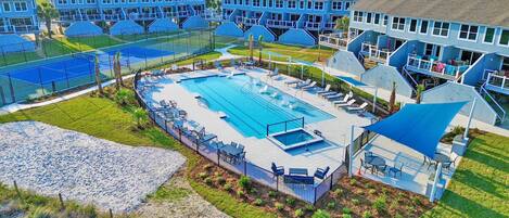Un resort con una piscina grande, tumbonas y una cancha de tenis.
