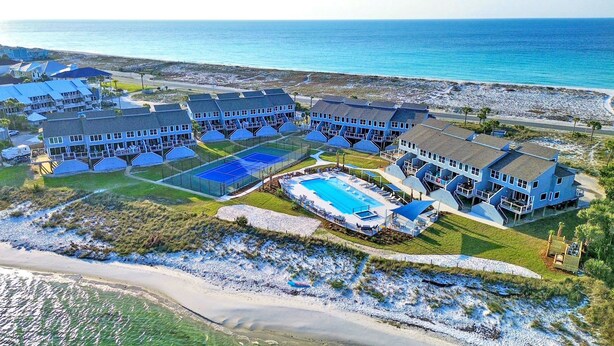 A coastal resort with multiple buildings, a large swimming pool, and a beach.