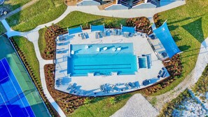 An aerial view of a swimming pool complex with multiple pools, sun loungers, and a tennis court.