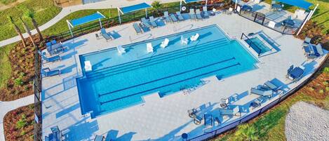 Una amplia piscina exterior con varias pistas, rodeada de tumbonas y sombrillas.