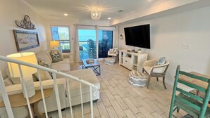 A living room with a sofa, coffee table, TV, and a balcony with outdoor furniture.