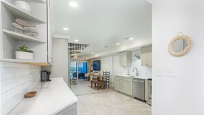 A modern kitchen with white cabinets, a white countertop, and a hexagonal tile floor. There is a dining area with a table and chairs, and a view of the city through large windows.