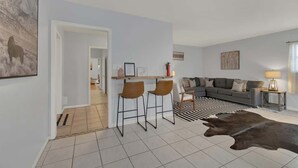 A modern living room with a sofa, two bar stools, a rug, and a cowhide rug. - Luxury Home 2-Mins to Downtown w/Sauna+Plunge Pool (Fredericksburg)