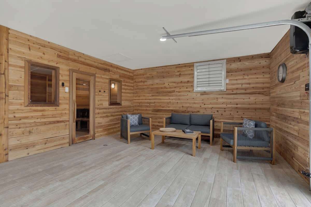 A wooden-paneled room with a sofa, two chairs, a coffee table, and a small table with a lamp.