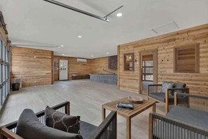 A spacious room with wooden walls and floors, a sofa, a coffee table, and a fireplace. - Luxury Home 2-Mins to Downtown w/Sauna+Plunge Pool (Fredericksburg)