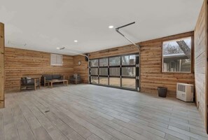 Une pièce spacieuse aux murs en bois, dotée d’une grande porte-fenêtre coulissante, d’un ventilateur de plafond et d’un système de climatisation intégré.