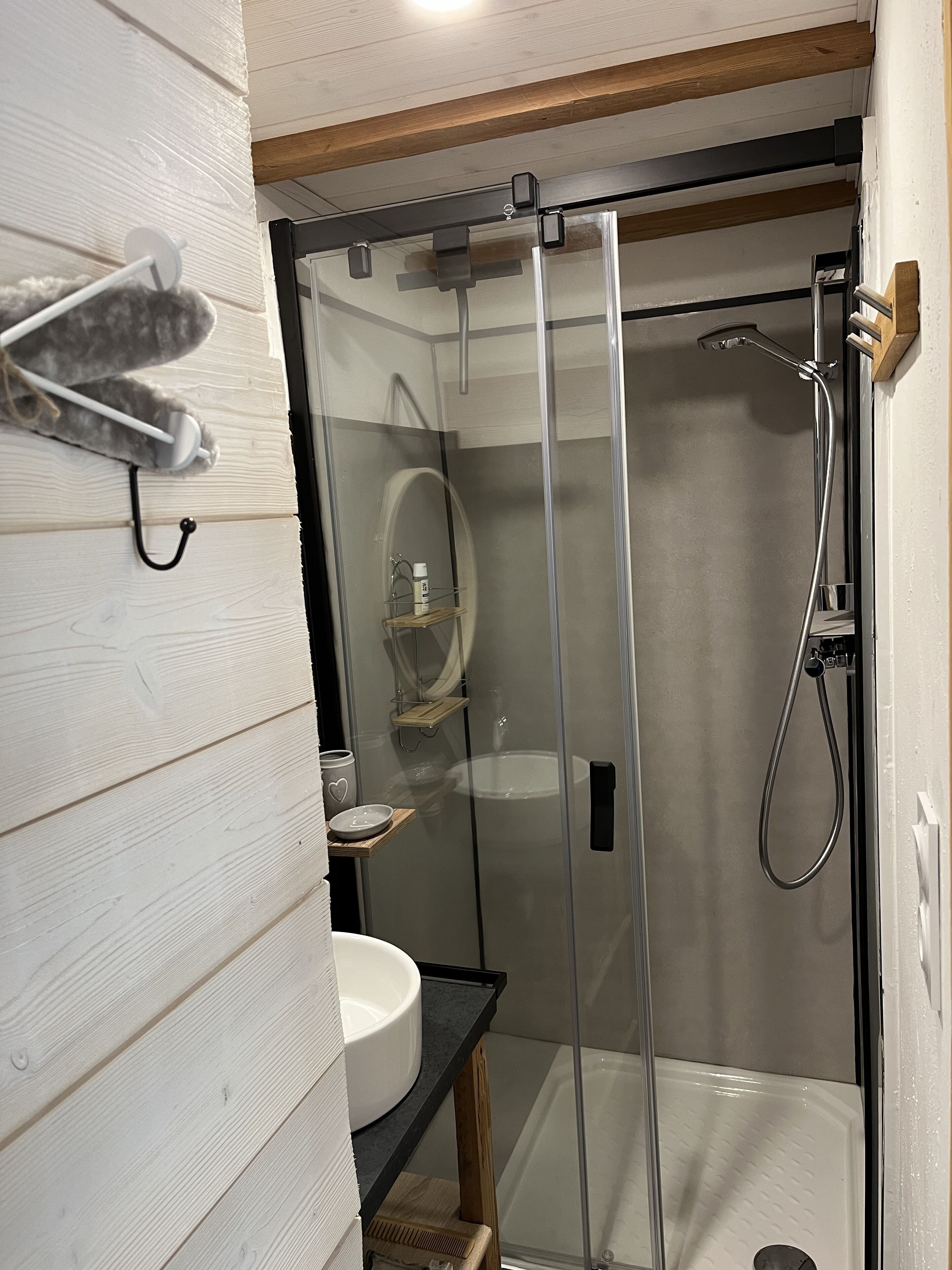 Un baño moderno con ducha de vidrio, lavamanos blanco y tocador de madera.