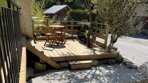 A wooden deck with outdoor seating, a small table, and a tree.