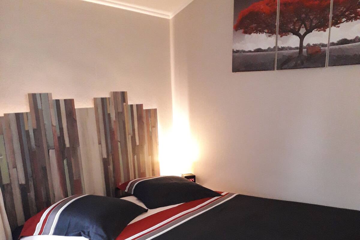 A bedroom with a bed, a nightstand, a wall clock, and a geometric-patterned rug.