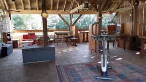 A rustic wooden structure with a metal-framed exercise machine, tables, benches, and a patterned rug. - Chambres d'hôtes de l'île du saule (Saumur)