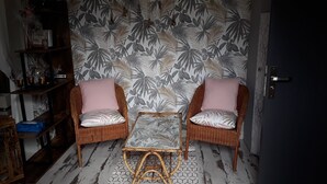 A room with two wicker chairs with cushions, a small table, and a patterned wallpaper. - Chambres d'hôtes de l'île du saule (Saumur)