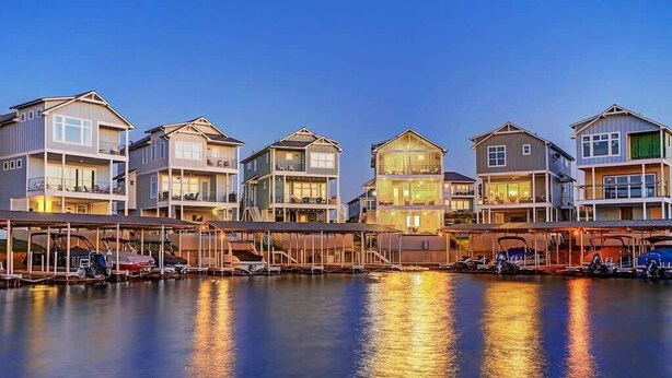 A waterfront property with multiple multi-story buildings, each featuring balconies and a covered dock area with boats.
