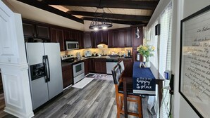 A kitchen with dark wooden cabinets, stainless steel appliances, a dining area with a blue tablecloth, and a decorative wall with a religious text. - Cozy property, a short walk to a lake front beach. (Locust Grove)
