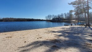 A lakeside view with a sandy beach, a dock, and a house across the water. - Cozy property, a short walk to a lake front beach. (Locust Grove)