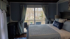 A bedroom with a large bed, a view through a sliding door to an outdoor balcony, and a painting on the wall. - Cozy property, a short walk to a lake front beach. (Locust Grove)