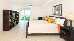 A bedroom with a large bed, a bookshelf, a nightstand, and a view of the ocean.