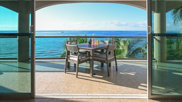 A balcony with a table and chairs, overlooking a body of water.