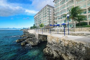 A coastal hotel with a balcony, palm trees, and a view of the sea.