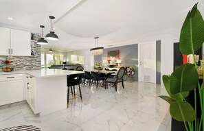 A modern kitchen with white cabinets, a marble countertop, and a dining area with a white table and black chairs.